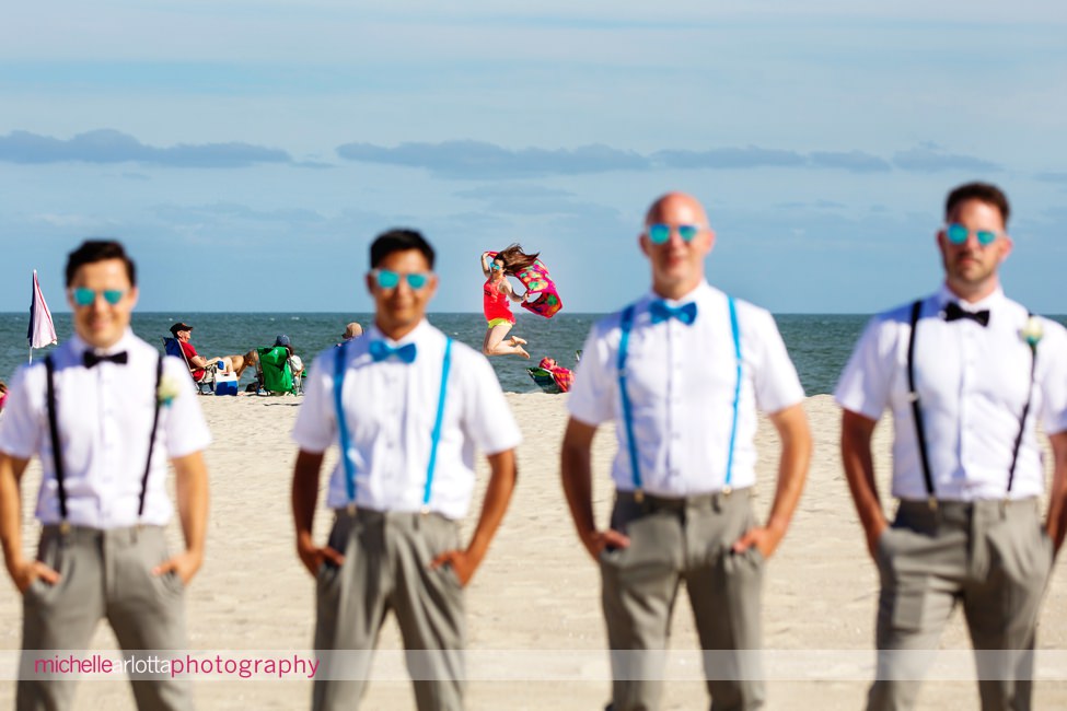 groomsmen smile as beachgoer jumps in background at cape may New Jersey wedding