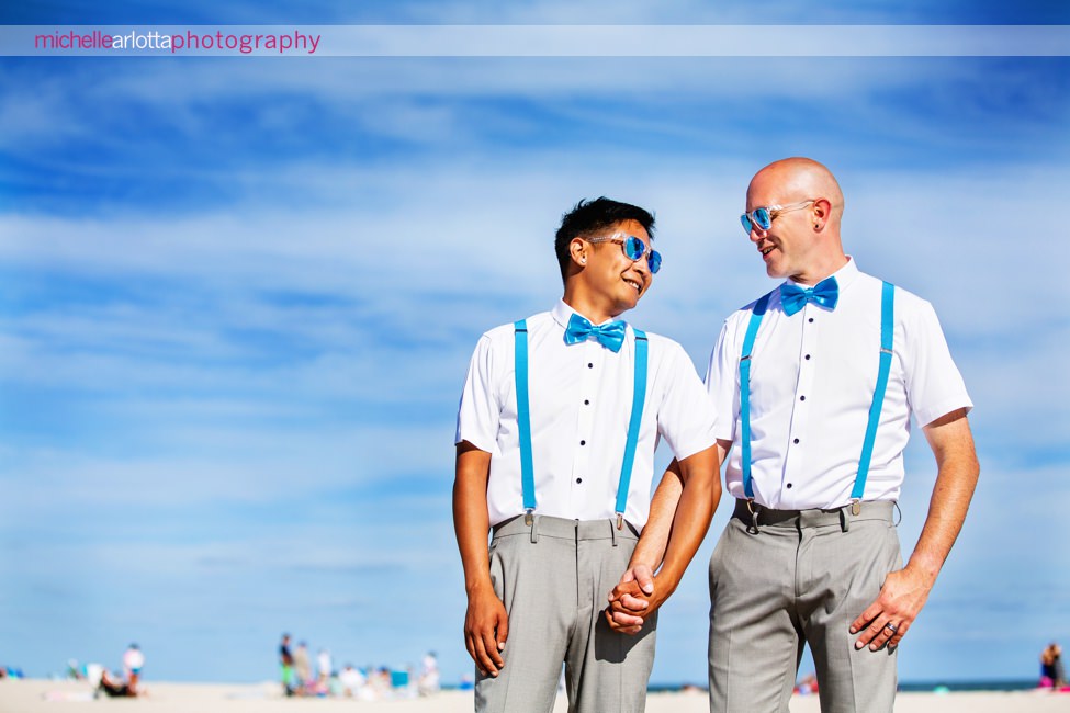 two grooms in blue bowties and blue suspenders smile together for portraits on the beach for their same sex grand hotel cape may wedding photographed by lgqbt friendly photographer Michelle arlotta