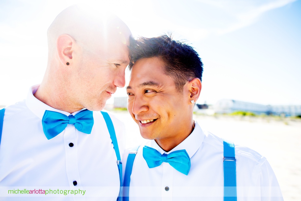 two grooms in blue bowties and blue suspenders smile together for portraits on the beach for their same sex grand hotel cape may wedding photographed by lgqbm friendly photographer Michelle arlotta