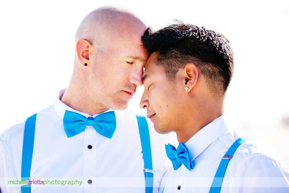 two grooms in blue bowties and blue suspenders smile together for portraits on the beach for their same sex grand hotel cape may wedding photographed by lgqbt friendly photographer Michelle arlotta
