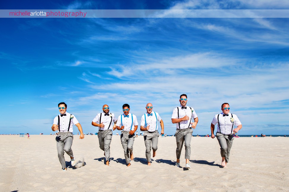 two grooms and their groomsmen run on the beach in cape may for grand hotel wedding