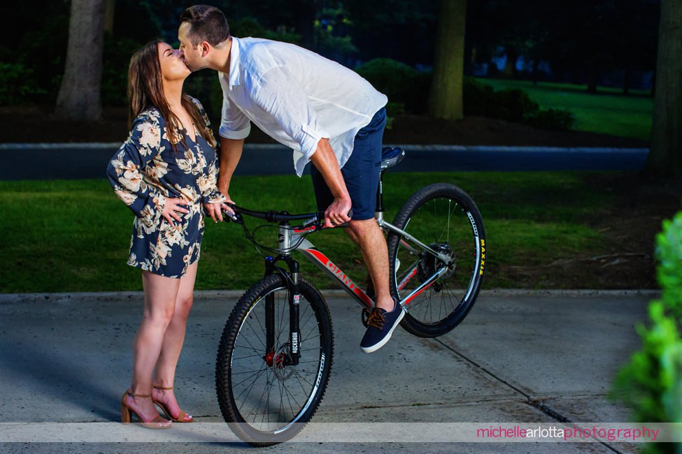 groom pops a wheelie as he kisses his bride during Monmouth university engagement sessionmichele and lawrence Monmouth university engagement session