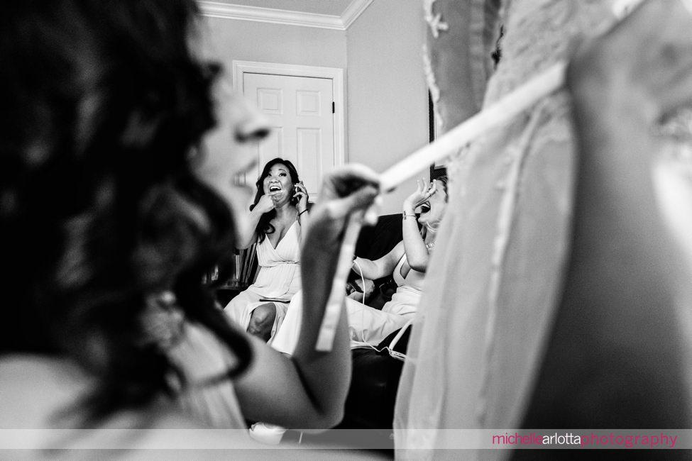 bridesmaids laughing in background while bride gets ready in nj