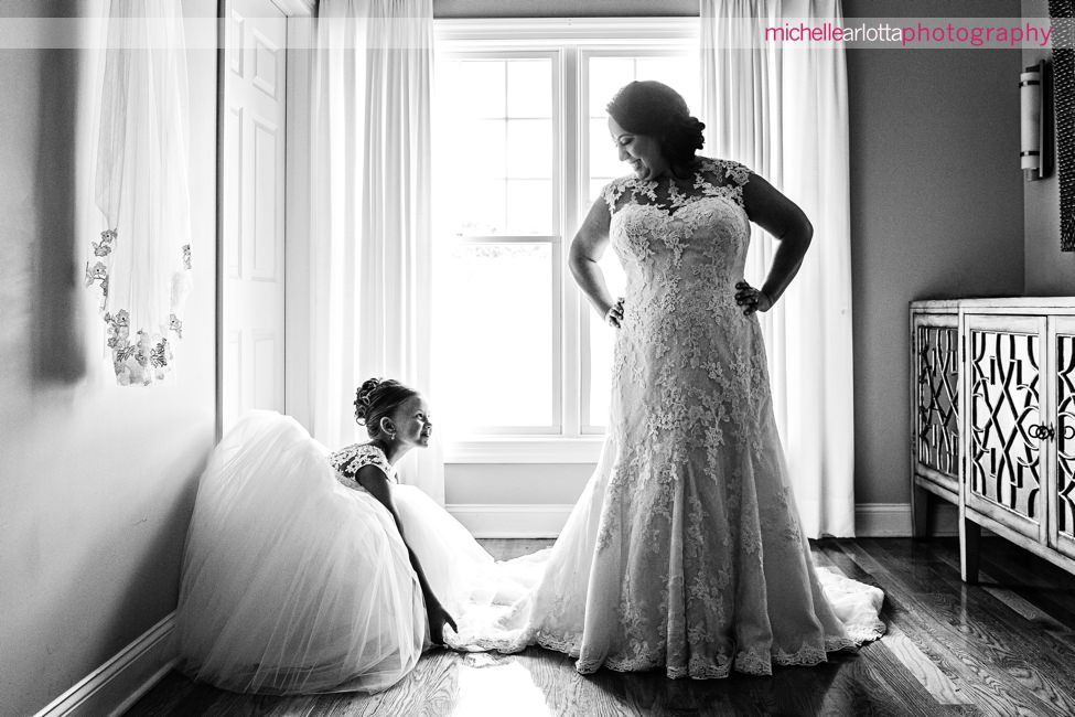 flower girl adjusts bride's pronovias wedding gown and smiles at her at New Jersey wedding captured by award winning New Jersey photographer Michelle arlotta