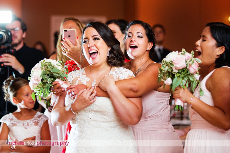 bride and bridesmaids embrace and sing along during groom and mother dance at bear brook valley new jersey wedding