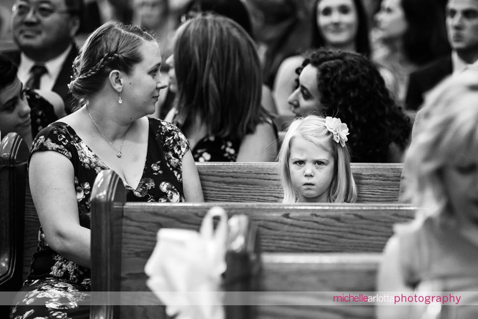 little girl in pews making a face at camera during New Jersey wedding