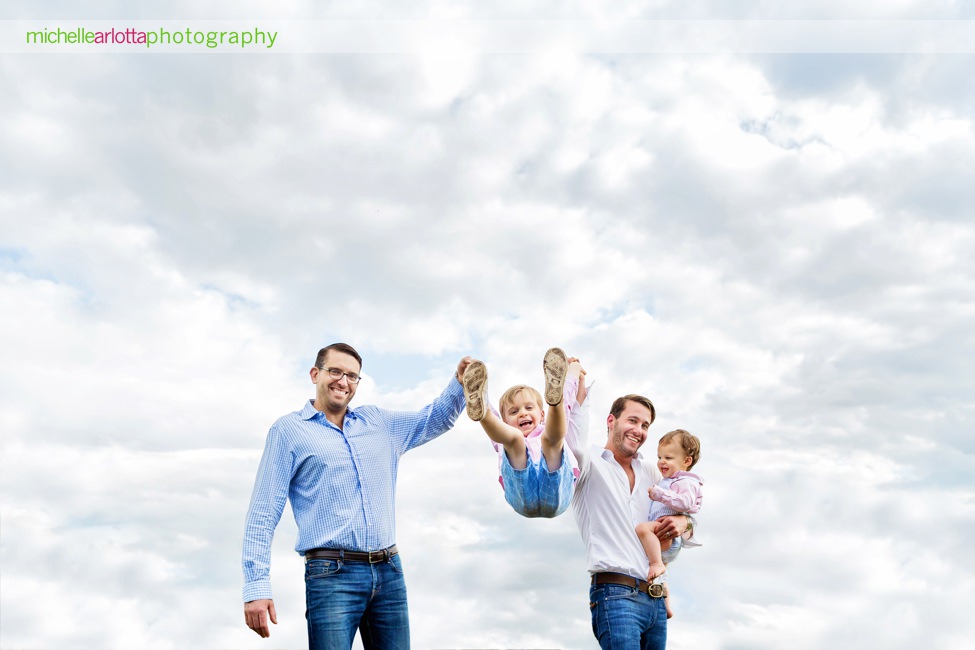 two dads swing toddler son up into air during nj family photography session