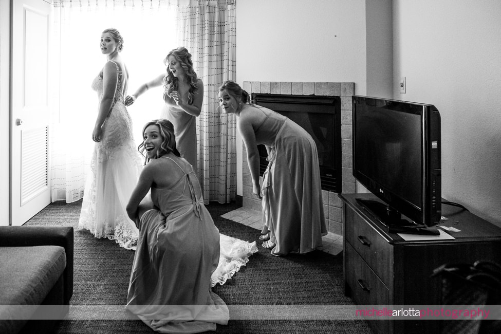 Waterloo village wedding bridesmaids all look back in laughter as they help bride into dress