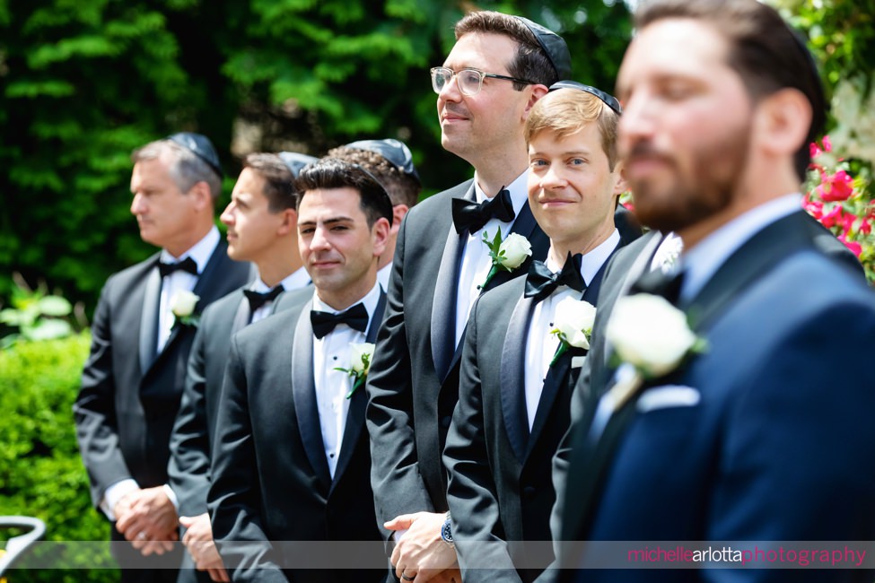 outdoor NJ wedding ceremony at Florentine Gardens groomsmen looks at groom as bride walks down the aisle