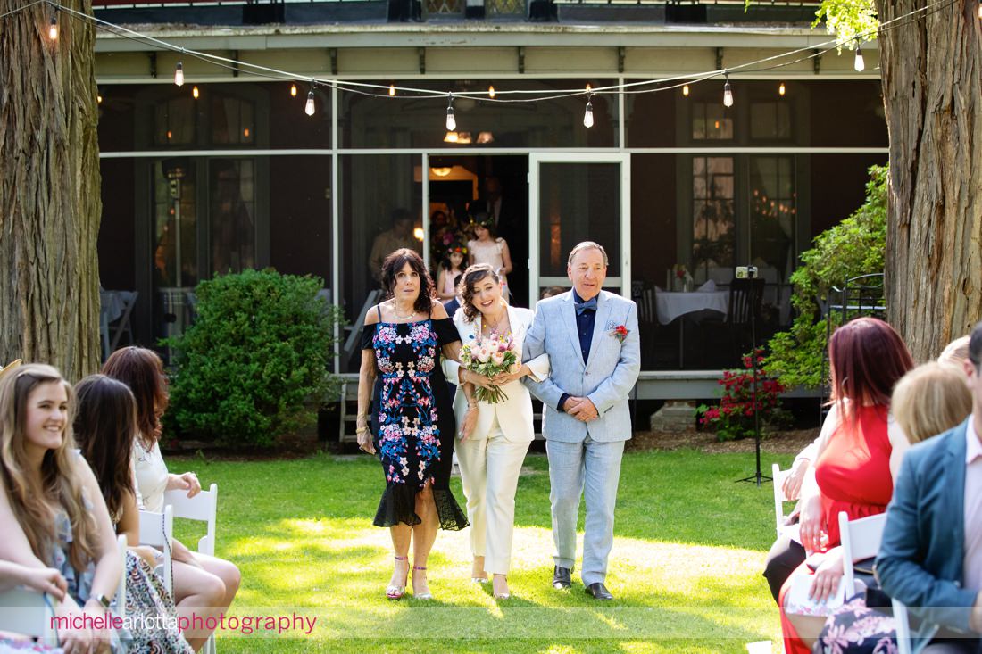 bride in Bindle and Keep suit walks down the aisle with her mother and father at Garvan's Gastropub New Paltz wedding