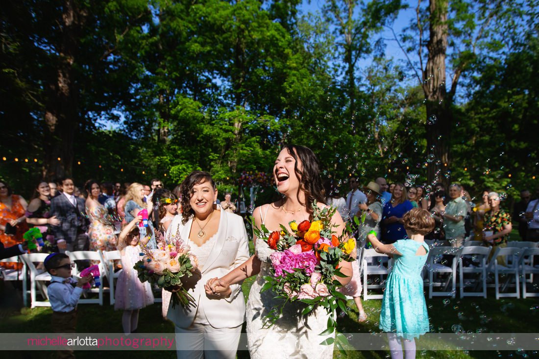 two brides exit outdoor wedding ceremony among bubbles at Garvan's Gastropub