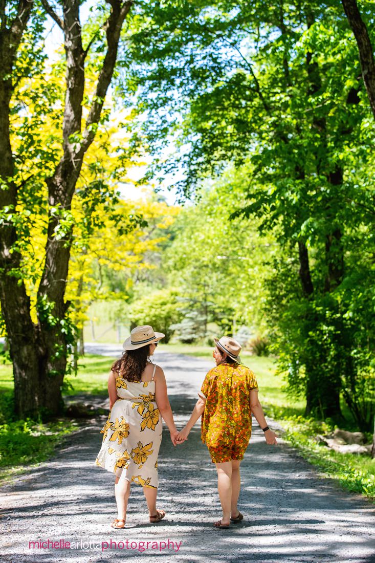 two brides-to-be walk down the road at Grateful Woods Kerhonkson NY Engagement Session with their dog following