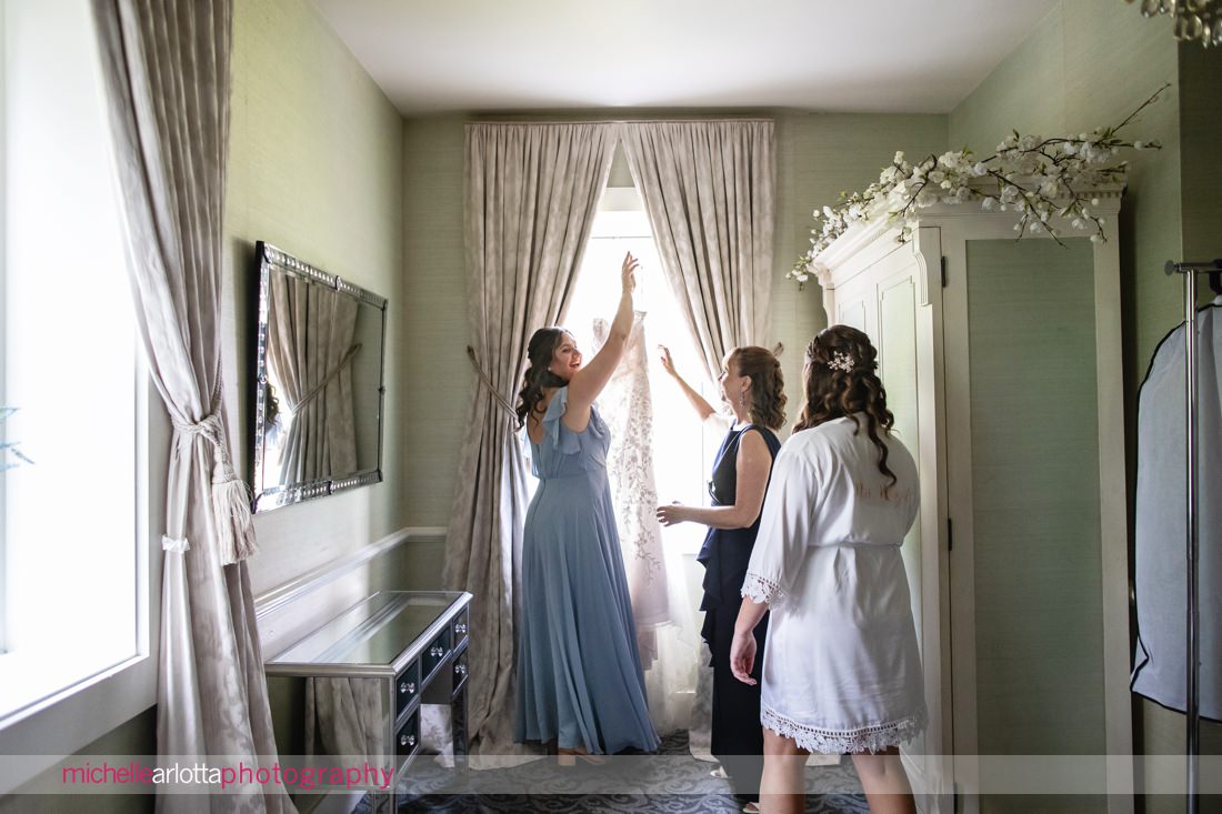 bridesmaid in sky blue dress helps bride get wedding dress off the hanger at Landmark Venues The Farmhouse
