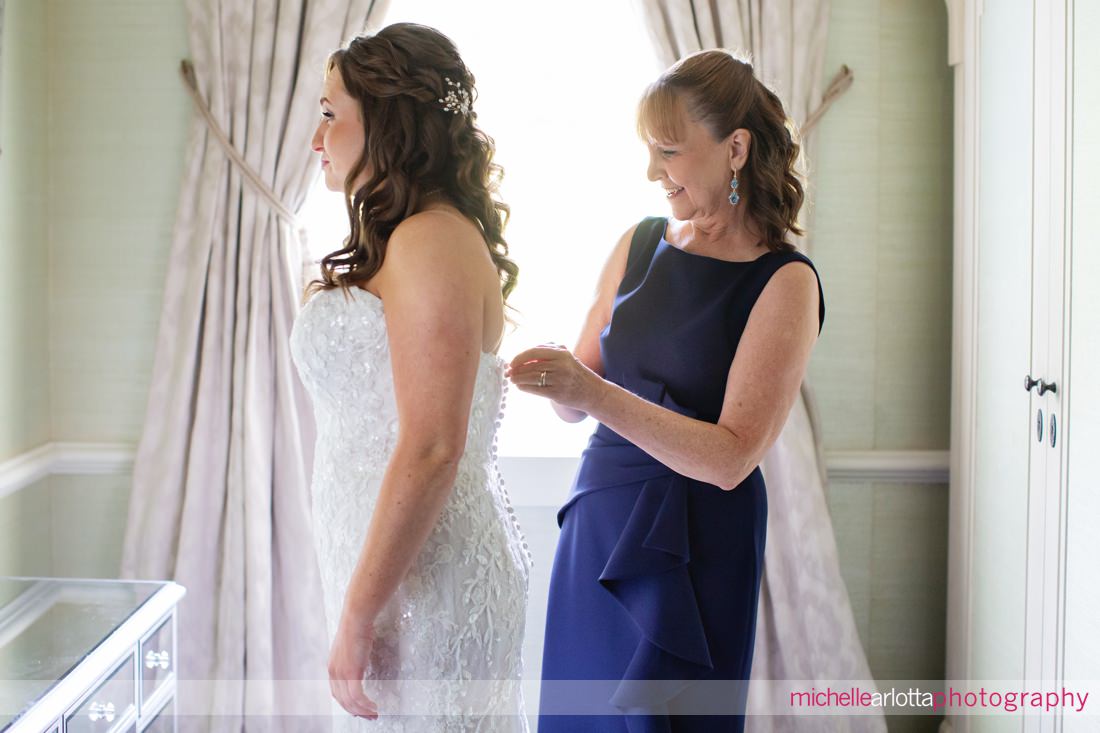 mother of bride in navy blue dress helps bride get into her dress at Landmark Venues The Farmhouse