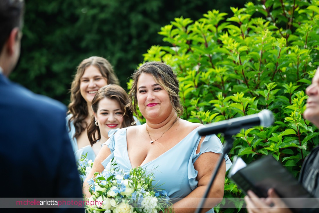 Outdoor ceremony at The Farmhouse NJ summer wedding bridesmaids smile while watching the wedding ceremony 