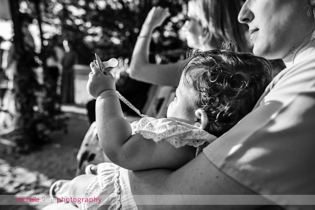 baby plays with pacifier and watches NJ Lake Mohawk Country Club lakeside wedding ceremony