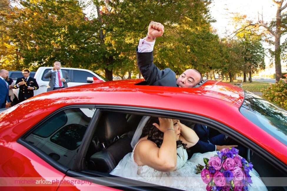 groom pumps fist out sunroof while bride checks hair in mirror of car at spring lake nj wedding