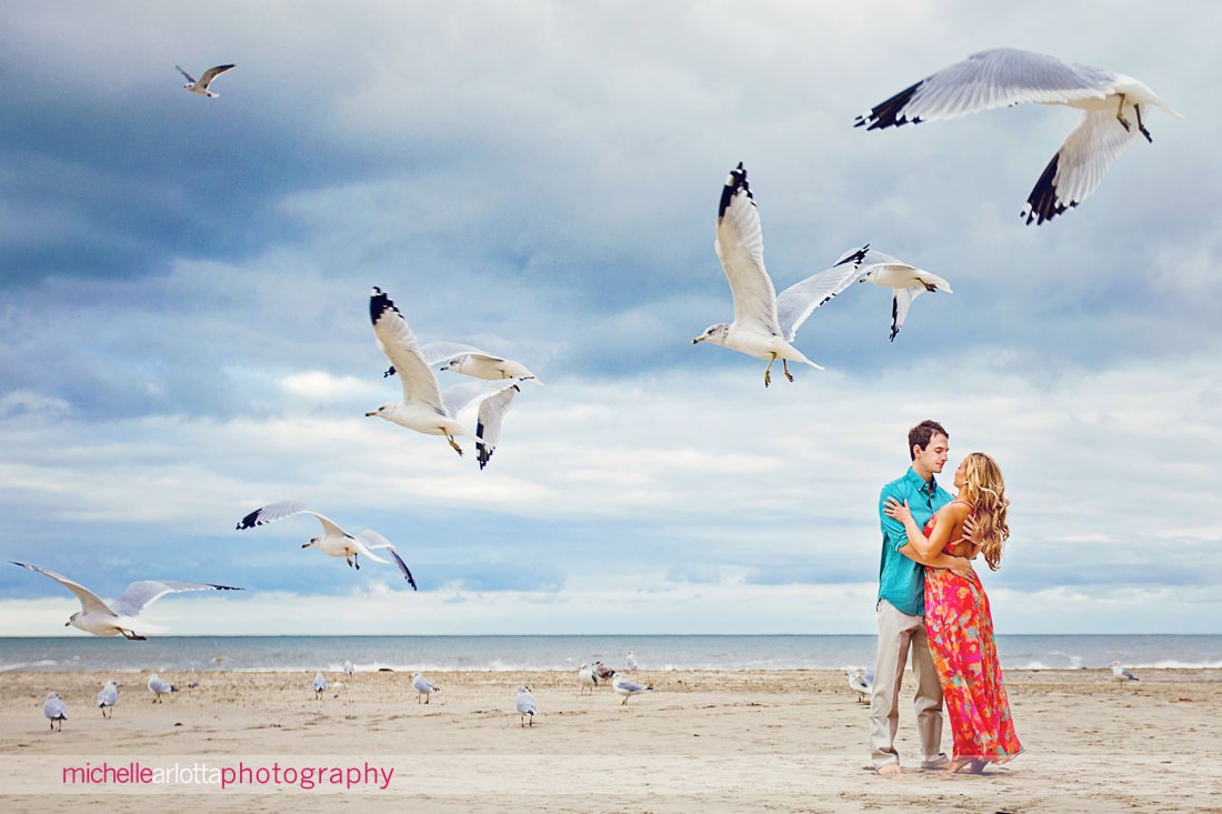 bride and groom embrace on beach as seagulls fly through the frame at long branch nj wedding