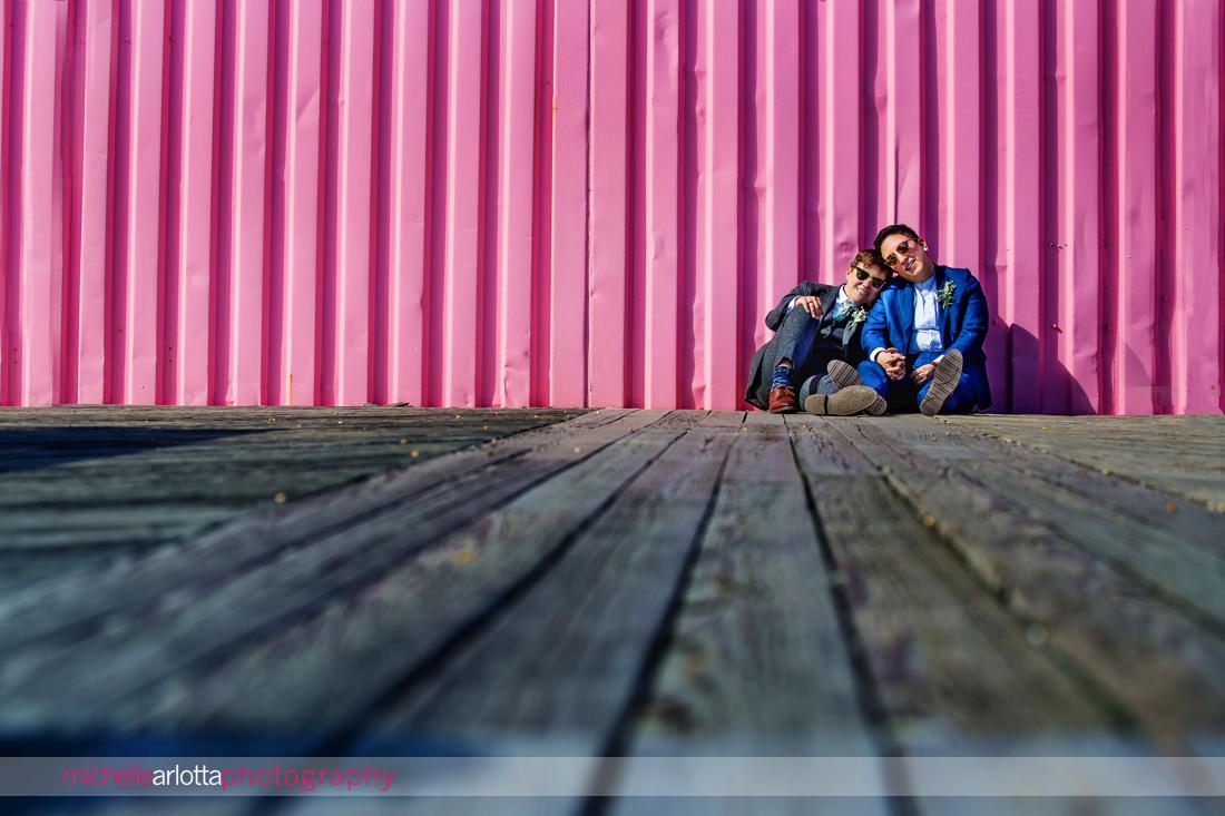 two brides in suits leaning against a pink shipping container during their asbury park nj wedding