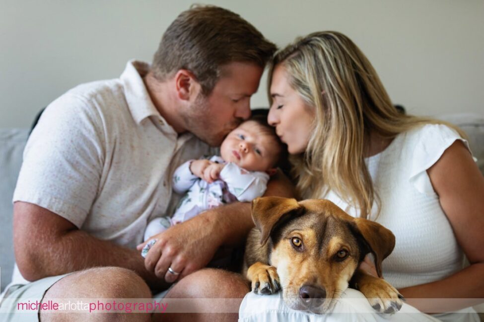 NJ newborn family photos parents kissing baby while dog looks at camera