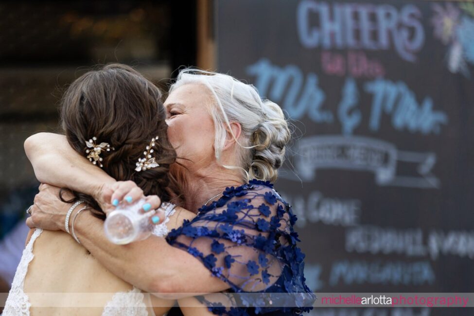 South Jersey Hammonton Summer Backyard wedding mother of the groom hugs bride in front of cheers sign on mobile bar