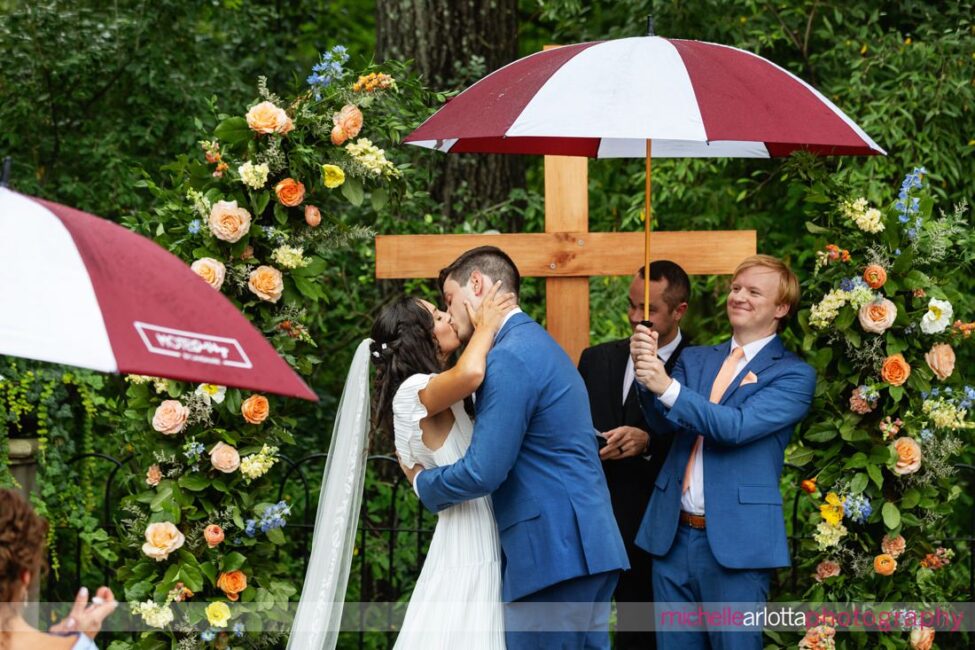 Landmark Venues Hotel Du Village New Hope PA outdoor wedding ceremony with umbrella being held over bride and groom during kiss