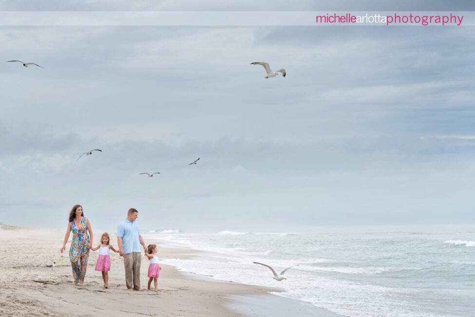 beach haven lbi nj family portrait session mom dad and two little girls walking on the beach with seagulls