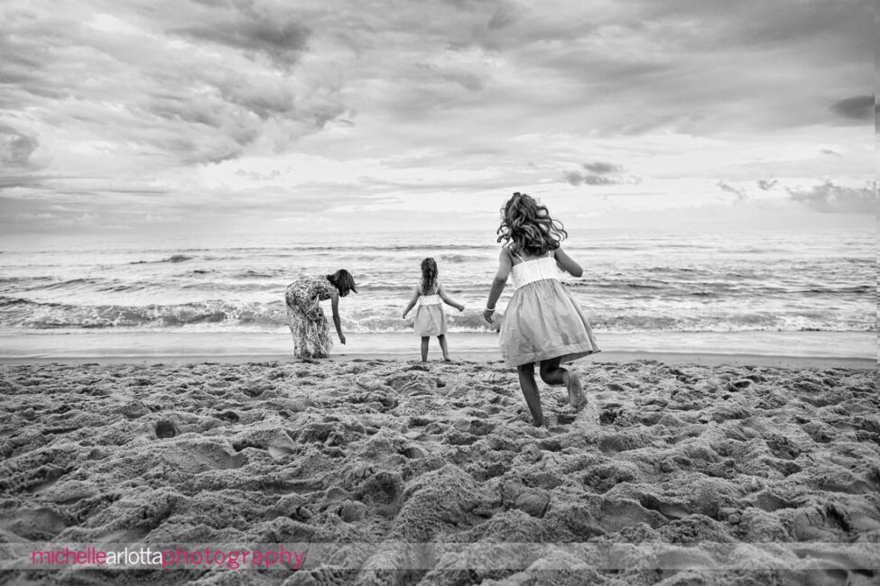 beach haven lbi nj family portrait session black and white image of little girl running toward mother and sister by the water