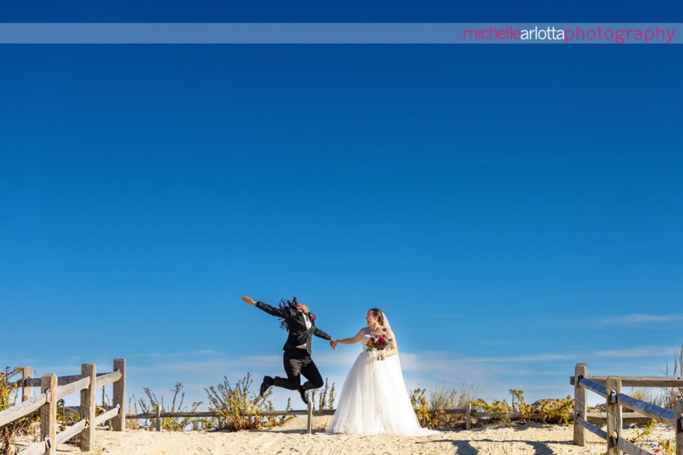 The Gables LBI New Jersey late fall bride in suit jumping while bride in white wedding gown watches on