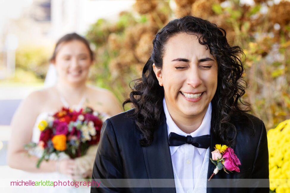 Bride in suit with bowtie laughs in anticipation of first look during Long Beach Island, Gables Inn NJ late fall wedding