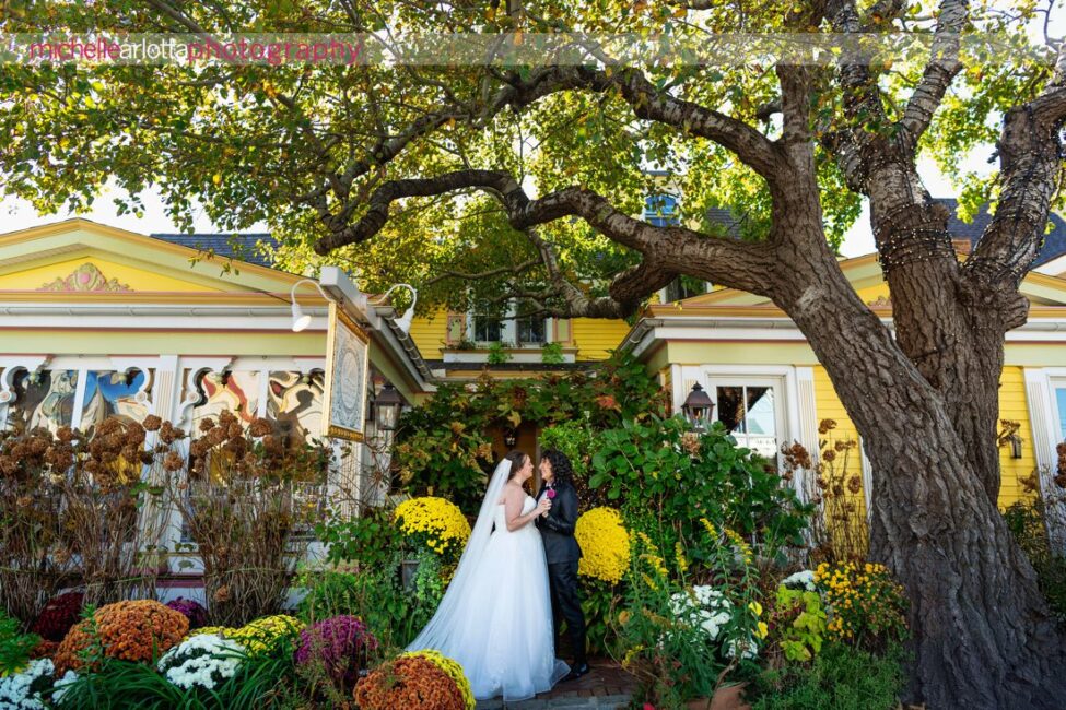 bride in white wedding gown with bride in black suit and bowtie in front of The Gables Inn for their Late Fall LBI NJ wedding