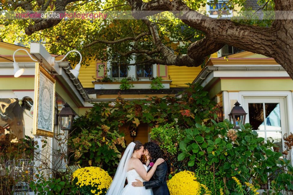 bride in white wedding gown with bride in black suit and bowtie in front of The Gables Inn for their Late Fall LBI NJ wedding