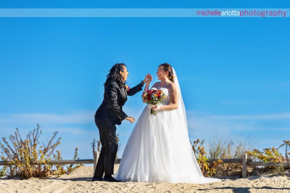 bride in white wedding gown with bride in black suit and bowtie at beach for Beach Haven, New Jersey wedding