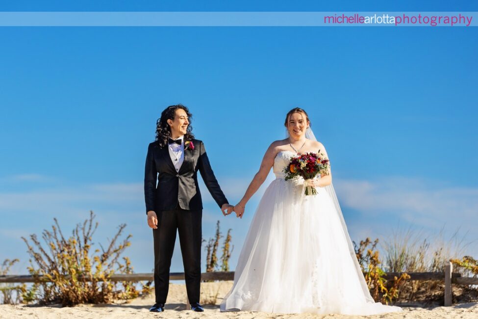 bride in white wedding gown with bride in black suit and bowtie at beach for Beach Haven, New Jersey wedding