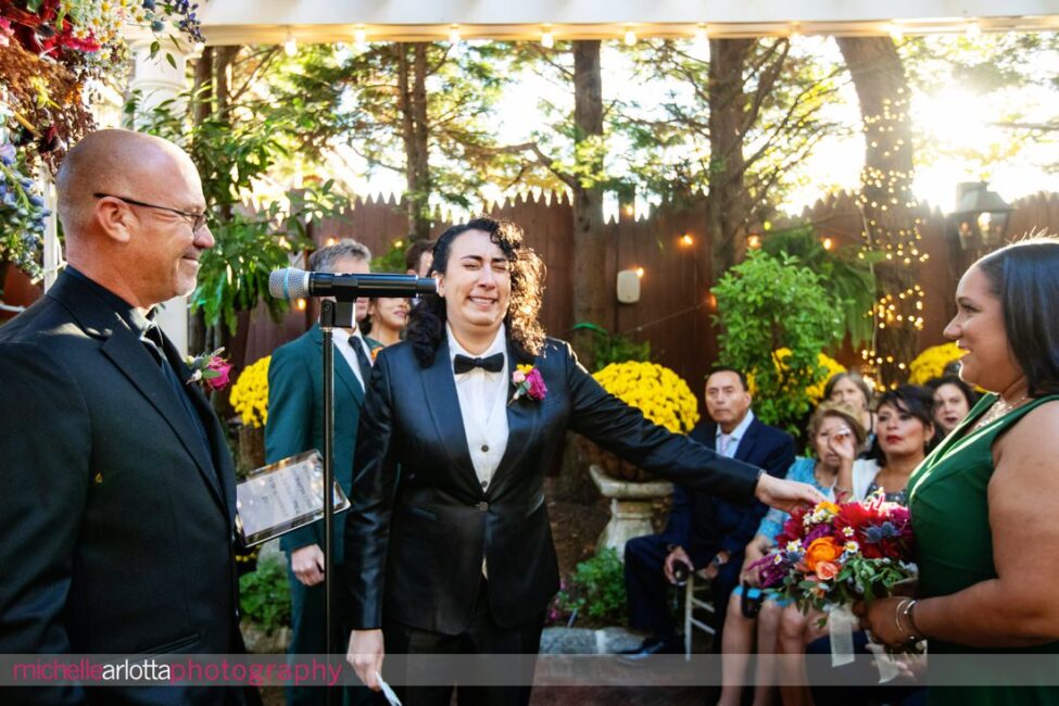 bride in black suit and black bow tie gets emotional as bride in white wedding dress starts to walk down the aisle at late fall gables lbi nj wedding