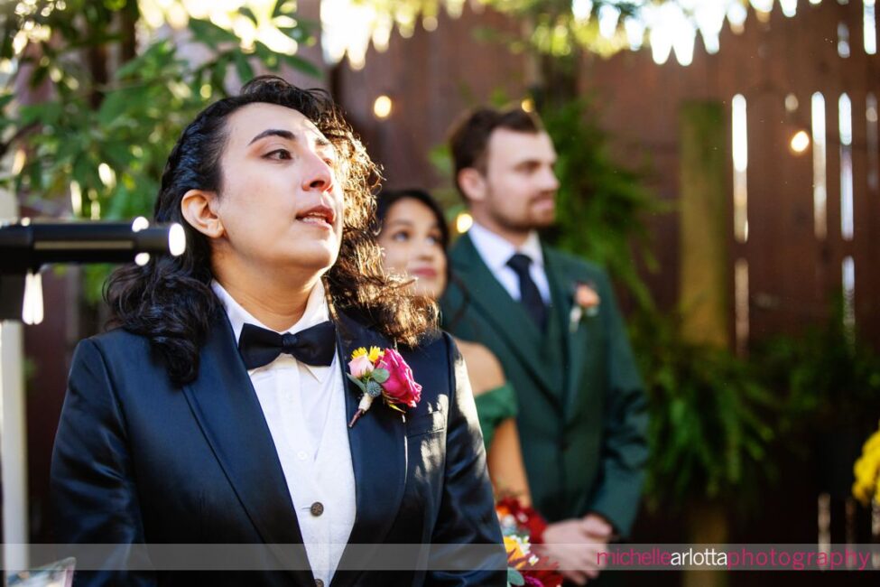 bride in black suit and black bow tie gets emotional as bride in white wedding dress starts to walk down the aisle at late fall gables lbi nj wedding