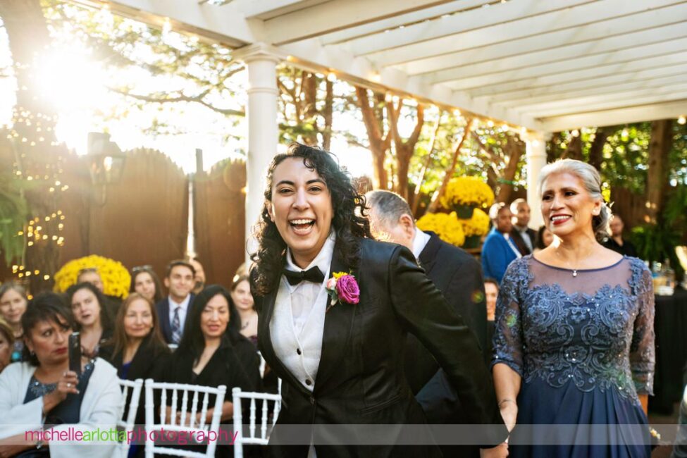 bride in black suit and black bow tie exuberant as she walks down the aisle during late fall gables lbi nj wedding