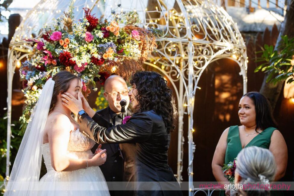 bride wipes tear away from other bride at altar during outdoor late fall garden wedding ceremony at Gables LBI New Jersey wedding