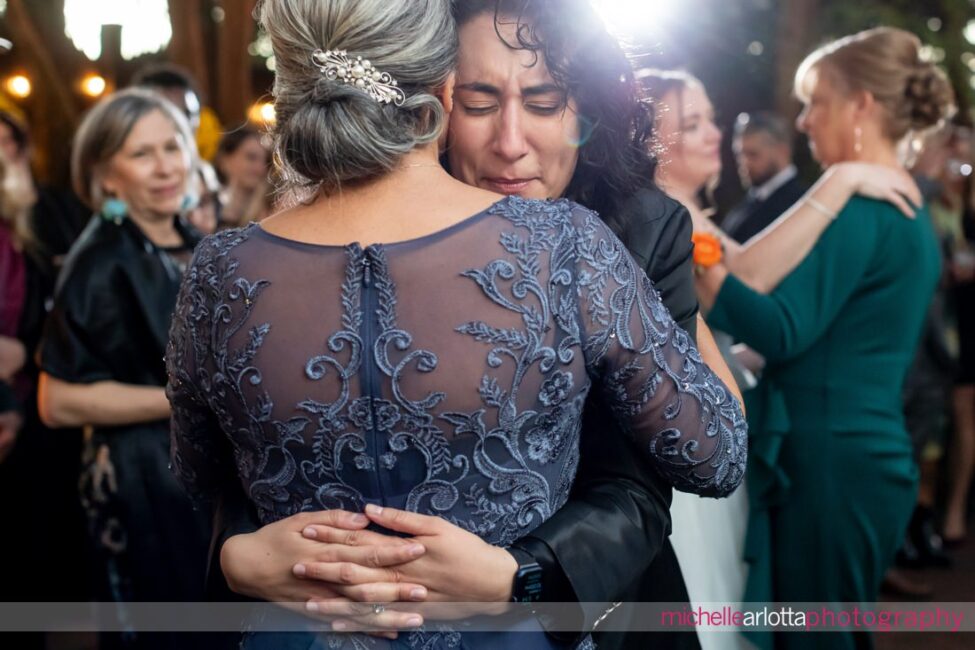 late fall outdoor garden wedding reception bride in black suit hugs mother and tears up while dancing with her mother at Gables Inn LBI NJ wedding