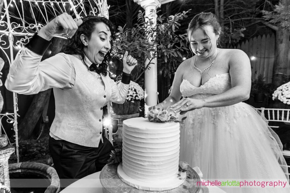 bride in bow tie excited to cut cake with bride in white gown at Gables LBI NJ wedding