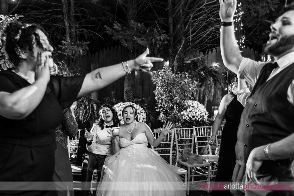 outdoor wedding reception guests dancing at late fall Gables LBI NJ wedding as two brides sit together on seats in the background singing