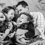 family of four laughs and giggles as the lie in the sand together during new jersey family photo session