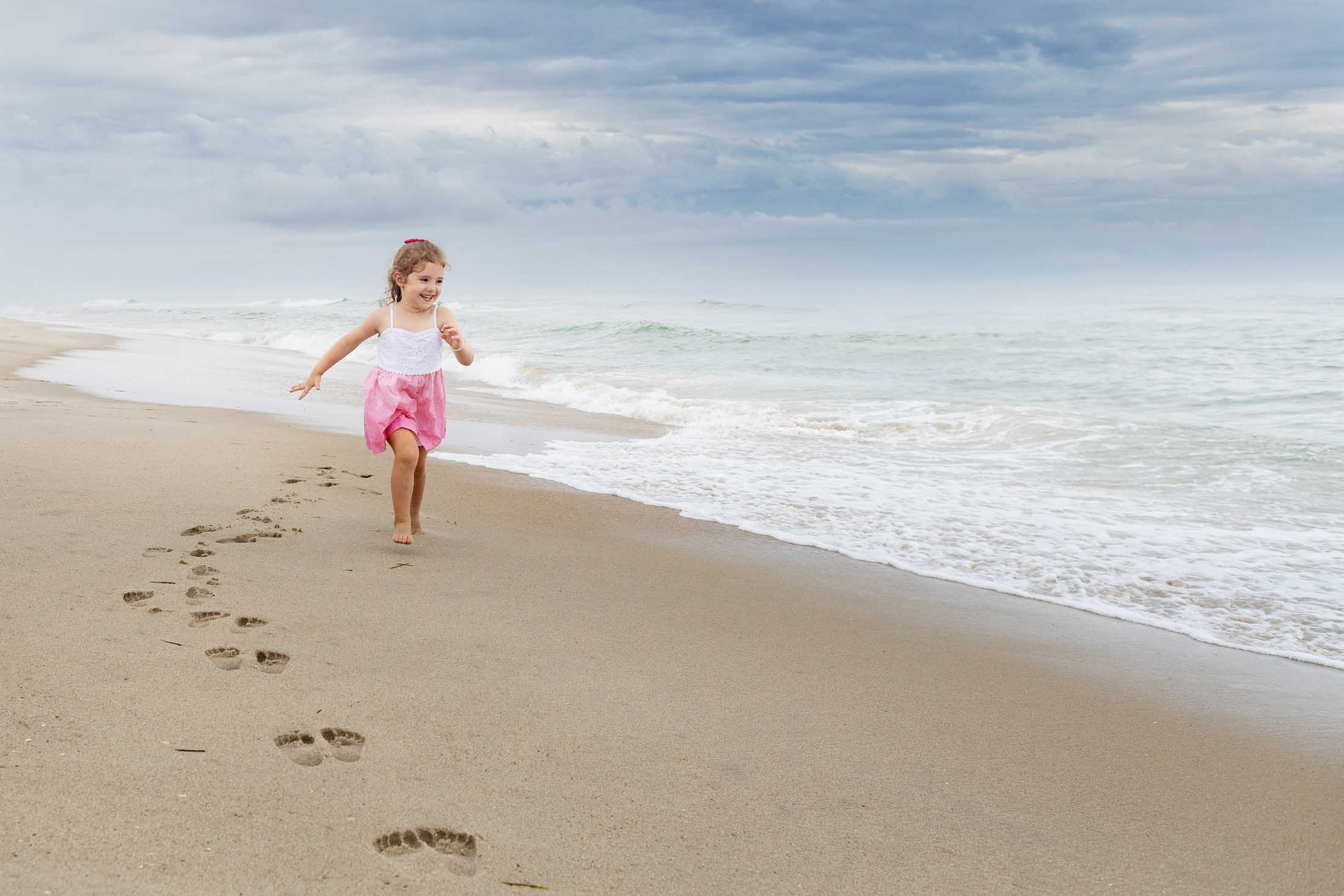 little girl runs on LBI beach with pink dress and footprints