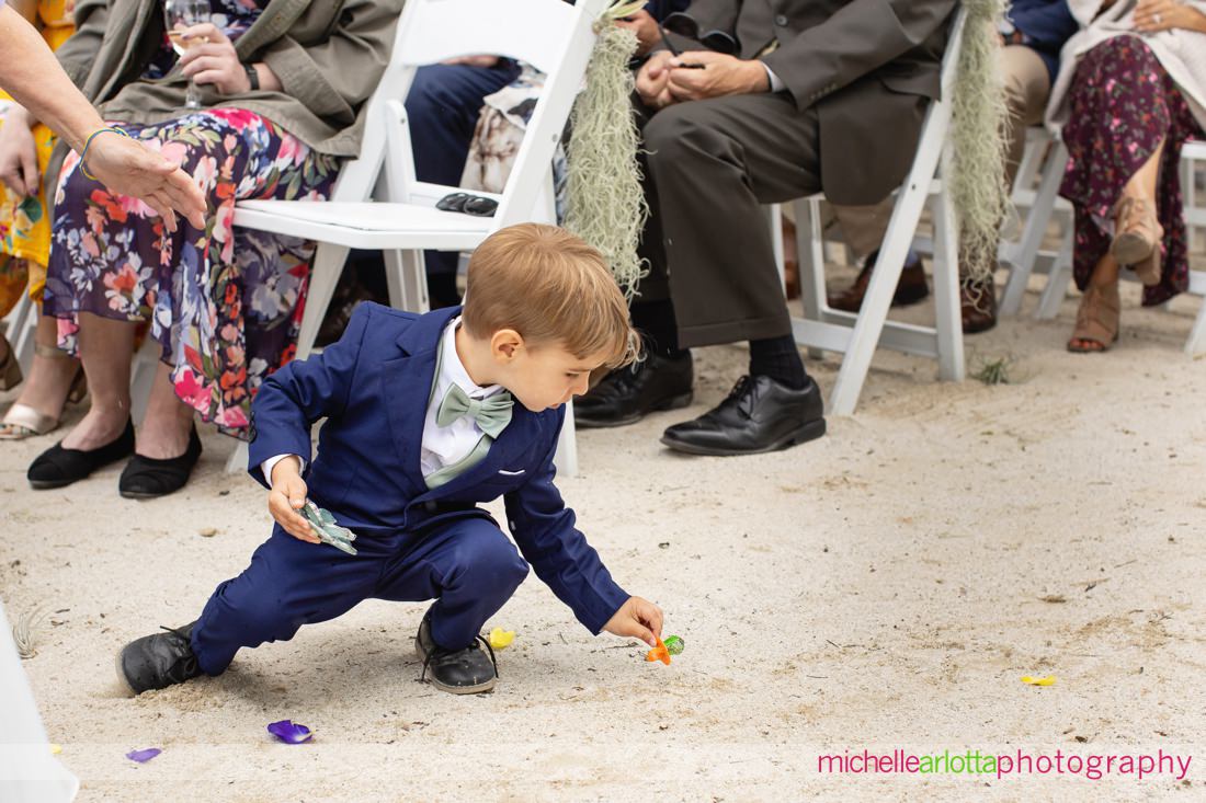 ring bearer drops ring pop as he walks down the aisle at Lake Mohawk Country Club lakeside wedding ceremony